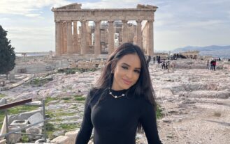 Woman with black shirt stands in front of historic ruins.