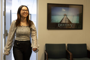 A woman walks into a room, On the wall hangs a picture with the word Destiny on it.