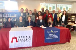 RCNJ and SCCC administrators sit at and stand behind a long table bearing the RCNJ and SCCC logos on table runners.