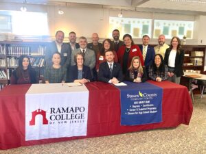 RCNJ and SCCC administrators sit at and stand behind a long table bearing the RCNJ and SCCC logos on table runners.