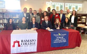 RCNJ and SCCC administrators sit at and stand behind a long table bearing the RCNJ and SCCC logos on table runners.