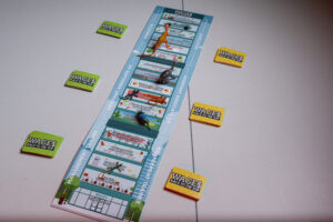 A board game sits on a table. There are dinosaur figures on top, and piles of cards to the side.