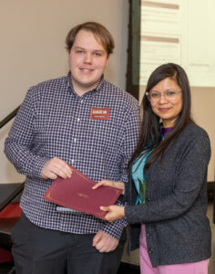 Two people stand together holding a maroon folder between them.