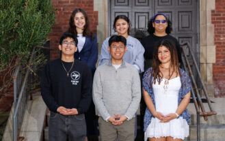 Six students are standing on stairs outside of Birch Mansion on campus. There are three in each of two rows.
