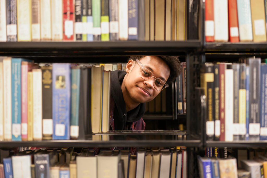 Jesiah Owens '26 is peeking through a shelf of books in the Potter Library on campus.