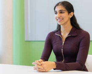 A young woman sits at a table and smiles.