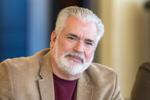 Don LaGreca is smiling at the camera in a tan blazer and maroon Ramapo College shirt.