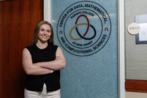 A young woman stands with her arms folded infront of a door with a symbol and the writing "Center for Data, Mathematical and Computational Sciences".