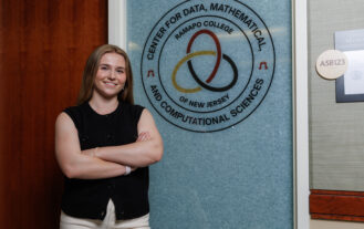 A young woman stands with her arms folded infront of a door with a symbol and the writing "Center for Data, Mathematical and Computational Sciences".