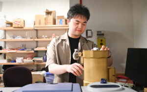 A young man stands and looks down at an engineering project in a lab.