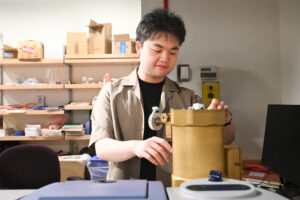 A young man stands and looks down at an engineering project in a lab.
