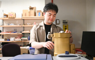 A young man stands and looks down at an engineering project in a lab.
