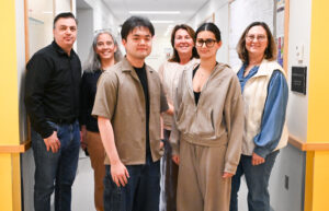 A group of six people, a mix of professors and college students, stand together in a hallway.