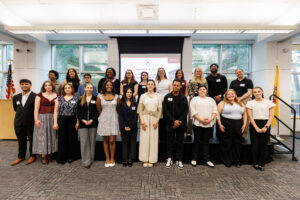 The graduating College Honors program students stand in two rows in front of a screen with the program logo at the 2026 College Honors Senior Symposium held on April 15, 2026
