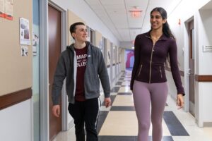 A man and a woman walk down a hallway together and smile at eachother.