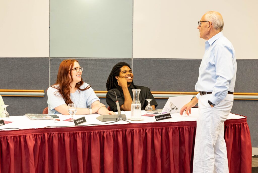 Sarah Glisson '26 and Kyree Robinson-Banks '26 sit at the Board of Trustees table speaking with Patrick O'Connor, vice president of government relations, who is standing to the right.