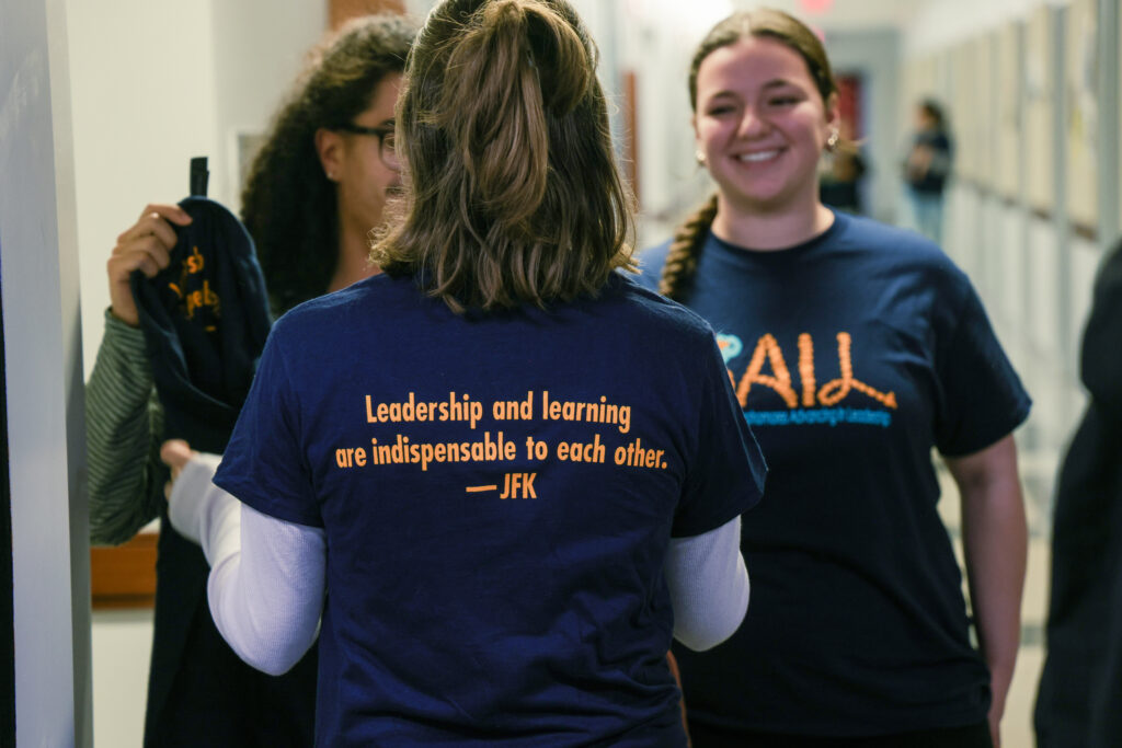 Sarah and classmates are talking, all wearing navy blue and gold Sophomores Advancing In Leadership (S.A.I.L.) t-shirts. 