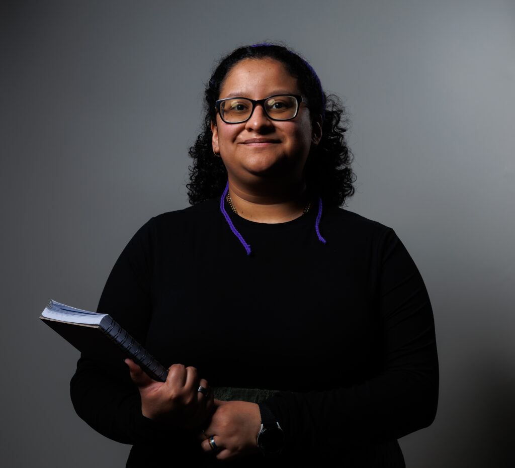 Bex Rodriguez is smiling and holding a wire-bound notebook in her right arm