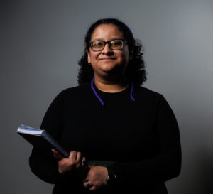 Bex Rodriguez is smiling and holding a wire-bound notebook in her right arm