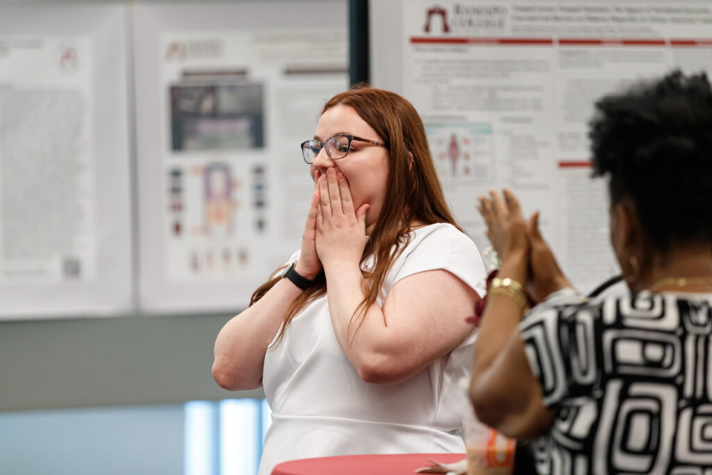 Sarah is holding her hands to her mouth as she hears the announcement of being named a Truman Scholar. 