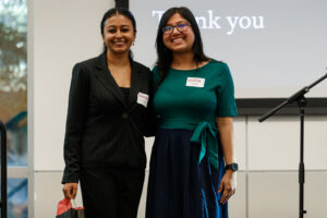 Two women stand shoulder to shoulder and smile.