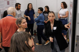 A young woman stands and points at a poster and talks. Others look on.
