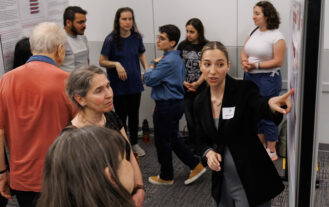 A young woman stands and points at a poster and talks. Others look on.