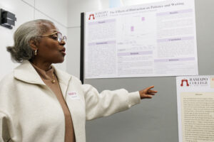 A senior citizen college students points at a research poster and speaks.