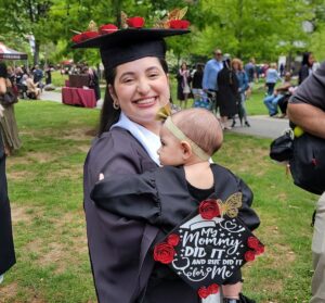 A woman in a graduation cap and gown holds a baby also with a graduation gown and a cap on her back.