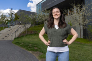 A woman stands outside with her hands on her hips and smiles.