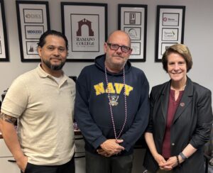 Three people stand side by side. A man in a polo shirt, a man in a sweatshirt that reads NAVY and a woman in a blazer. 