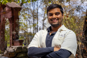 A man stands outside with his arms crossed and smiles.