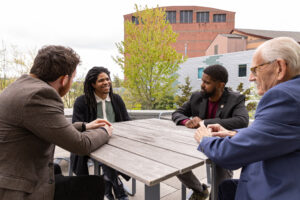 Four men sit around a table outside.