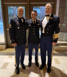 Three men in military dress uniforms stand inside and smile.