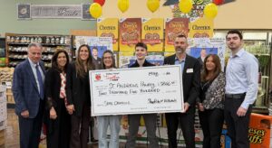 Eight people stand side to side in a supermarket holding a large check.
