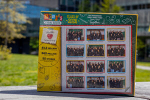 A Cheerios box with pictures of teams of people is on concrete outside.