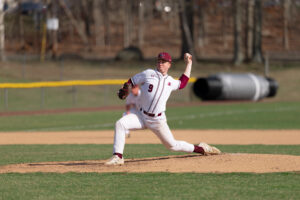 A young man in a white and maroon baseball untiform pitches a baseball from the mound.