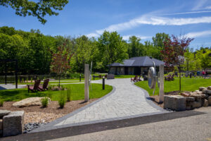 A path of pavers leads to a small building. Maroon chairs are in the surrounding grass.