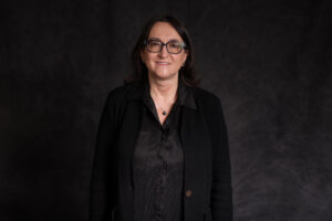 A woman wearing black stands against a black background.