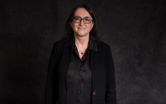 A woman wearing black stands against a black background.