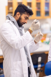 A student in a white lab coat is piping liquid into a vile in one of the bio labs on campus.