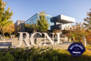 The image is the exterior of the RCNJ Learning Commons on a clear, fall day. The large RCNJ metal sculpted letters are in the foreground with a blue sky and several trees in various shades of green, orange, and yellow in the background and on both sides of the frame
