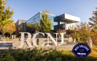 The image is the exterior of the RCNJ Learning Commons on a clear, fall day. The large RCNJ metal sculpted letters are in the foreground with a blue sky and several trees in various shades of green, orange, and yellow in the background and on both sides of the frame
