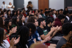 Young people sit in chairs and listen.