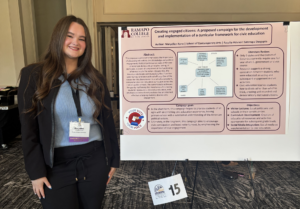 A woman stands next to a poster with text and smiles. She is inside.
