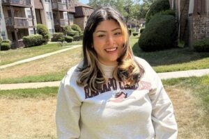 A woman wearing a Ramapo sweatshirt stands outside and smiles.