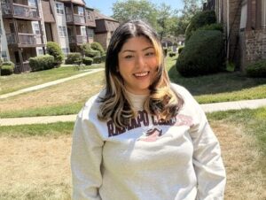 A woman wearing a Ramapo sweatshirt stands outside and smiles.