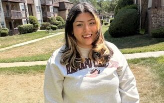 A woman wearing a Ramapo sweatshirt stands outside and smiles.
