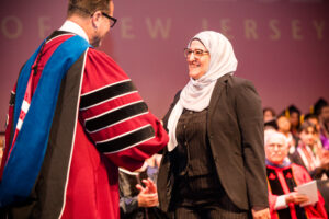 A woman smiles as she shakes the hand of a man in a graduation gown.
