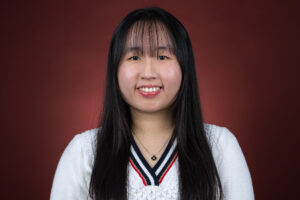 A woman smiles at the camera. There is a red background behind her.